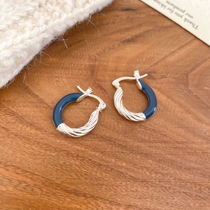 Detail of silver twisted metal and blue enamel hoop earrings on a rustic wood surface