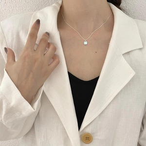 Detailed view of a silver teardrop pendant with light blue stone on a woman's neckline