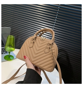 Detail of beige shell bag featuring V-shaped quilted texture and gold metal zippers