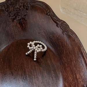 Macro detail of S925 sterling silver beaded bow ring on a vintage carved wooden tray