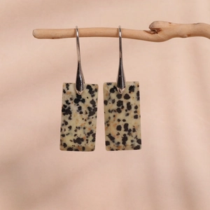 Detailed view of beige spotted rectangle stone drop earrings hanging on a wood branch