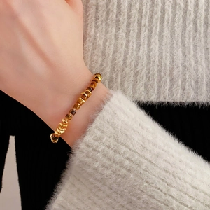 Close-up of golden tiger eye beaded bracelet worn by a model on a knitted sweater sleeve