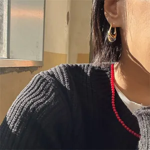 Primo piano di orecchini a U dorati minimalisti con goccia in resina su una modella.