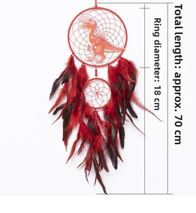 Detail of red dream catcher featuring a green dinosaur and natural hanging feathers