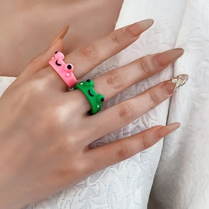 Close-up of vibrant cartoon frog rings in pink and green on model hand