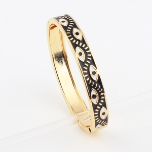 Detail of gold plated evil eye bangle with black enamel dripping oil and clasp closure