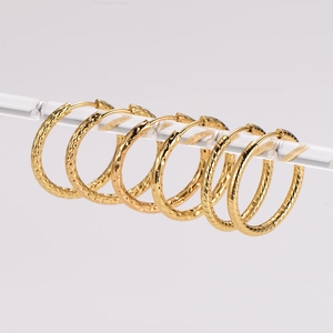 Three pairs of vintage gold hoop earrings with hammered and twisted textures on clear stand