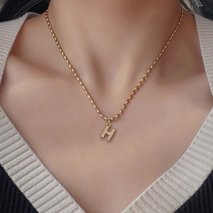 Close-up of golden beaded chain necklace with a zircon-encrusted 'H' letter pendant