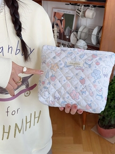 Quilted white cosmetic bag with cute cartoon patterns held by a person in a cozy kitchen