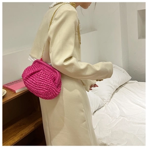 Magenta woven straw crossbody bag with golden chain strap worn by a model in a bedroom