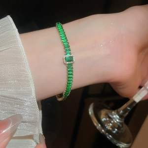 Dettaglio di un elegante bracciale dorato con zirconi verde smeraldo sul polso di una modella