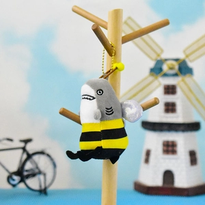 Funny shark plush keychain with bee costume hanging on a wooden stand for gift ideas