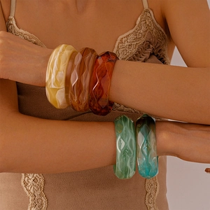 Close-up of retro acrylic geometric bangles in amber and emerald tones worn by a model