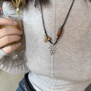 Detail of bohemian wooden grape pendant on black woven cord worn over gray knitwear