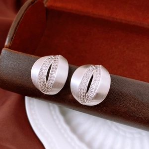 Macro view of C-shaped matte silver earrings with micro-set cubic zirconia crystals