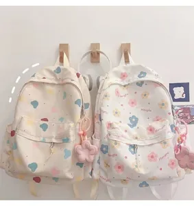 Close-up of cute cartoon printed backpacks in cream color with floral plush pendants