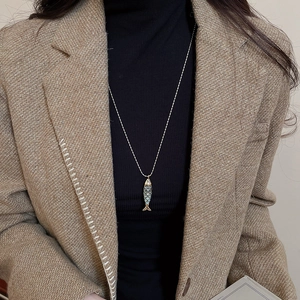 Detail of fish pendant necklace with blue enamel on golden chain worn with winter coat