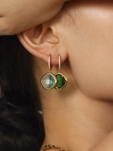 Gros plan de boucles d'oreilles dorées avec zircons carrés bleu et vert sur un mannequin