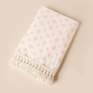 Detail of baby muslin cotton blanket with pink bow print and delicate fringe trim edges