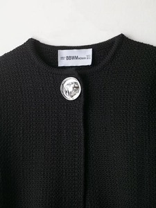 Detail of a textured black knit cardigan featuring a decorative silver relief button