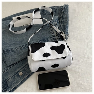 Detail of a cow print crossbody bag with flap closure and matching strap on white background