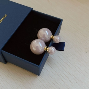 Detail of double-sided champagne pearl earrings on a premium blue jewelry box cushion