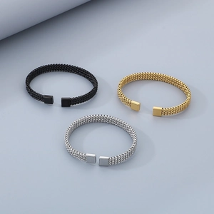 Macro shot of three C-shaped braided steel wire bracelets in gold, silver and black