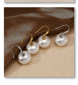 Detailed view of large white round pearl earrings with gold and silver hooks on ceramic tray
