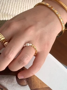 Detail of stacked gold bangle with sparkling cubic zirconia and pearl ring on model