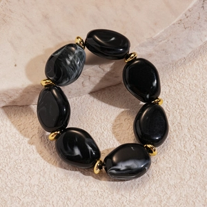 Detail of irregular black ink acrylic beads and gold spacers on a marble surface