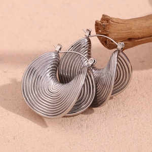 Detail shot of silver irregular ripple earrings on textured wood for a stylish metal look