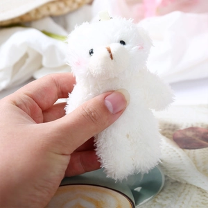 Close-up of a mini white plush teddy bear charm with pink blush details and a hanging loop