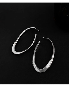Macro shot of large silver oval hoop earrings with polished metal finish on black background