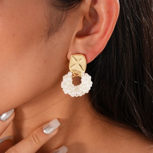 Close-up of gold metal and white pearl drop earrings worn by a model in a high-end style