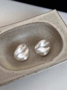 Macro shot of silver textured geometric stud earrings on a beige ceramic tray