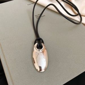 Close-up of polished silver oval pendant on black cord necklace against grey book background