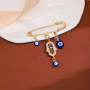 Detailed macro view of golden Hamsa hand brooch with blue evil eye charms and rhinestones