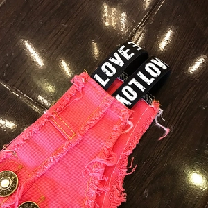 Dettaglio degli shorts di jeans rosa con bottone metallico e nastro elastico con scritte