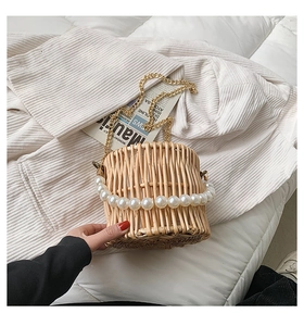 Detail of woven straw bucket bag featuring pearl top handle and gold metal chain strap