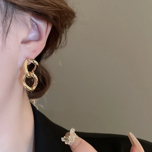 Close-up of geometric interlocking gold chain link earrings worn on a model ear
