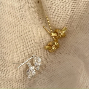 Minimalist knot earrings in S925 silver and gold finish on beige linen fabric