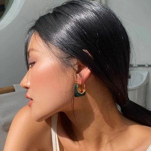 U-shaped green resin and gold metal hoop earrings worn by a model in natural light