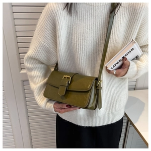 Detail of dark green oily leather shoulder bag with gold buckle on a white sweater