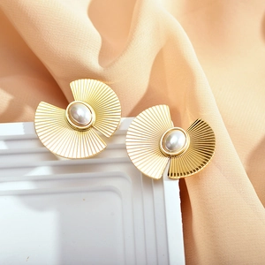 Macro shot of gold metal flower earrings with white pearls on soft peach silk fabric