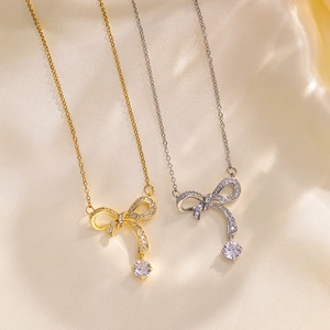 Elegant gold and silver bowknot necklaces with zircon pendants on soft silk background