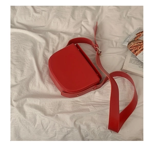 Detailed top view of a red vintage saddle bag with wide strap on cream fabric