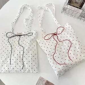 Detail of white canvas tote bags with heart prints and decorative bow ties on a desk