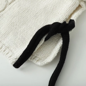 Detail of white chunky knit sweater featuring contrasting black faux-fur tie accents
