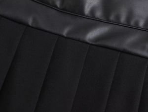 Macro detail of black faux leather spliced with pleated fabric on women's shorts skirt