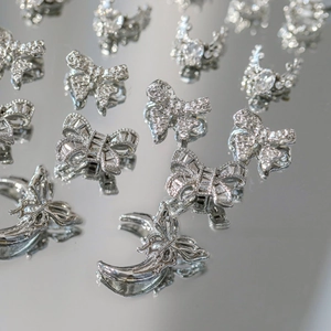 Détail de bijoux d'ongles argentés en forme de nœud et lune avec zircons sur miroir